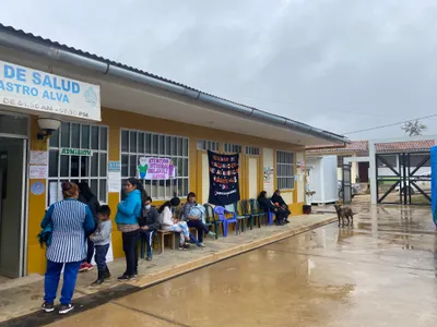 An image of a public health building on a cloudy day, with a number of people waiting outside. There are banners relating to health topics and a dog visible in the foreground.